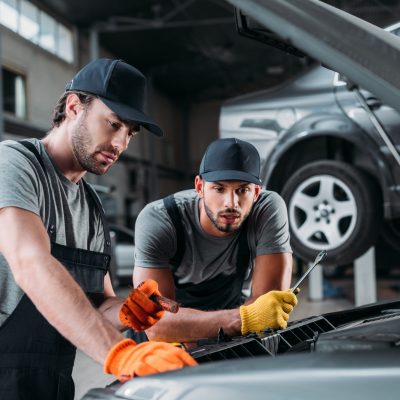 professional manual workers repairing car in mechanic shop